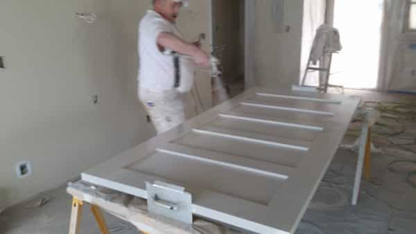 man painting doors with paint sprayer